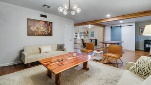 Ein Wohnzimmer mit einem Holzesstisch, einer Couch und einer Küche im Hintergrund.