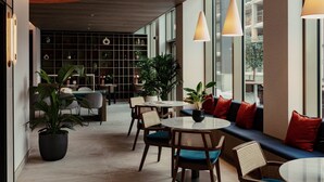 A modern indoor space with seating areas, tables, and potted plants. - Urban Rest Stratford (London)