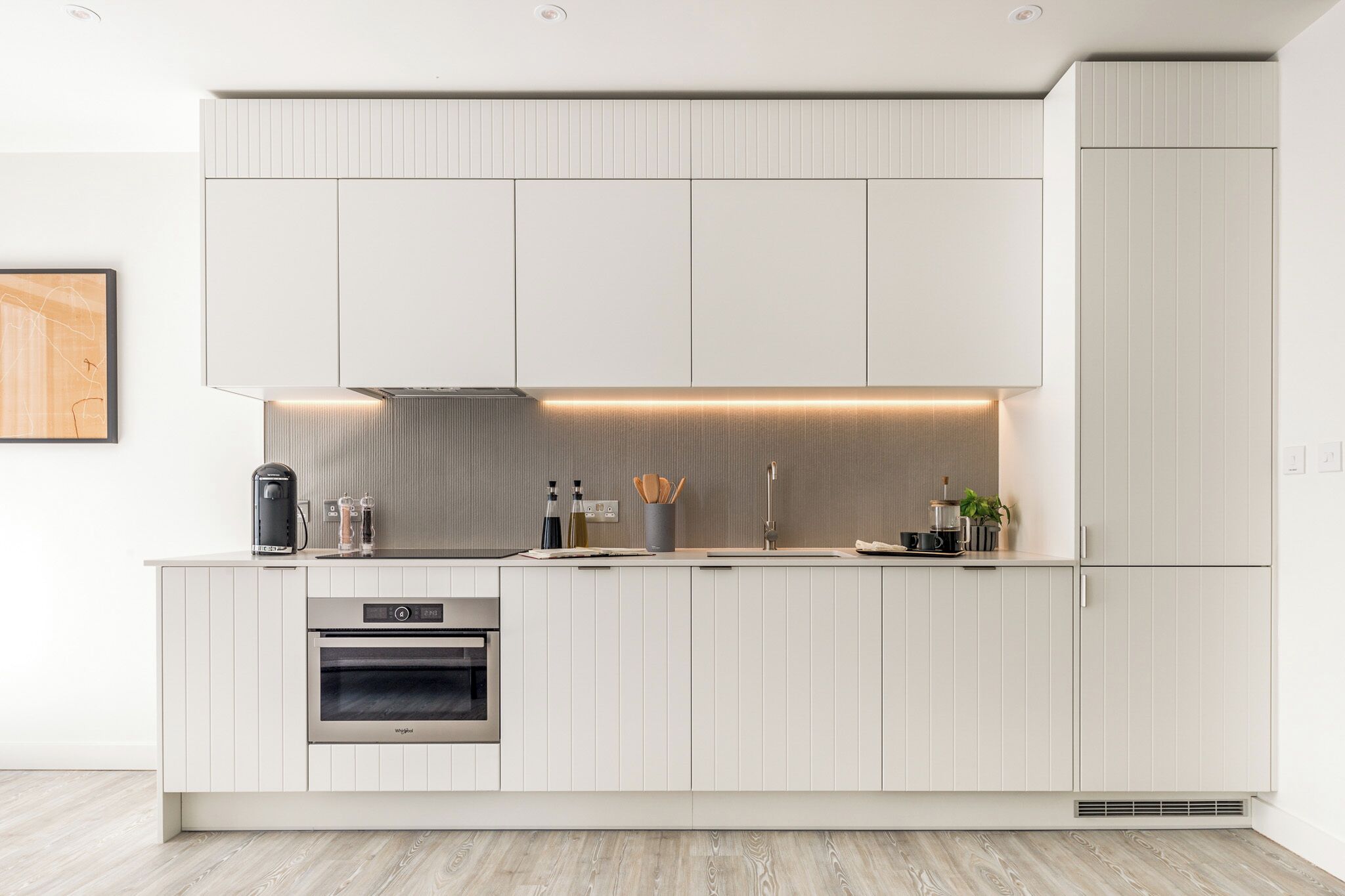 A modern kitchen with white cabinetry, a built-in oven, and a countertop with various appliances and utensils.