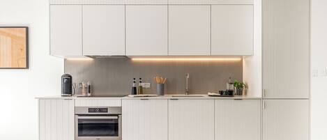 A modern kitchen with white cabinetry, a built-in oven, and a countertop with various appliances and utensils.