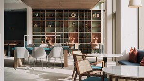 A modern interior with a dining area, seating, and a wall of shelves with decorative items. - Urban Rest Stratford (London)