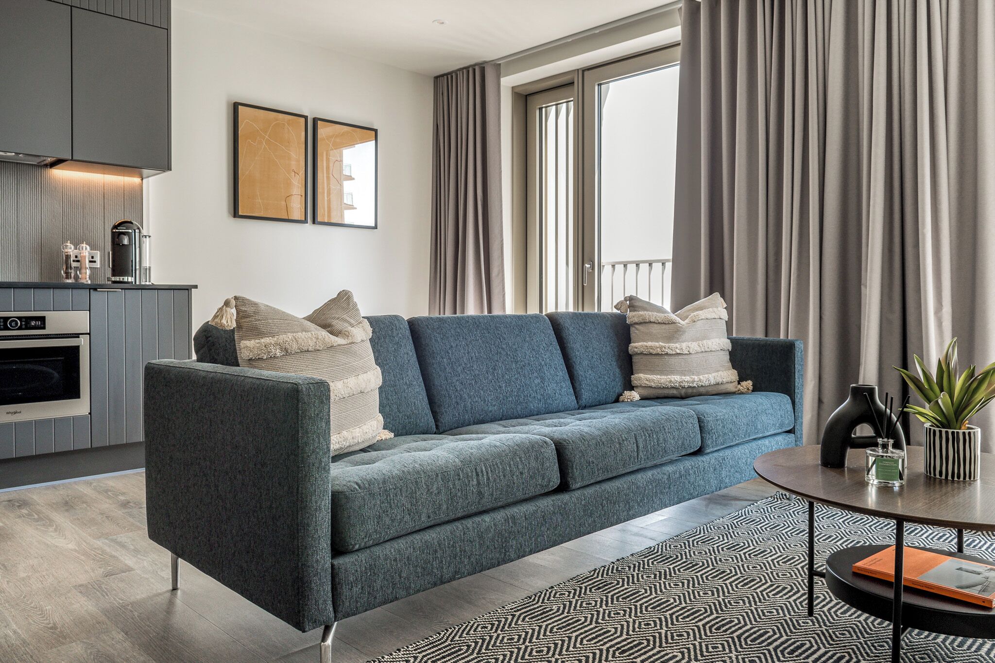 A modern living room with a grey sofa, a coffee machine, and a dining table with a plant.