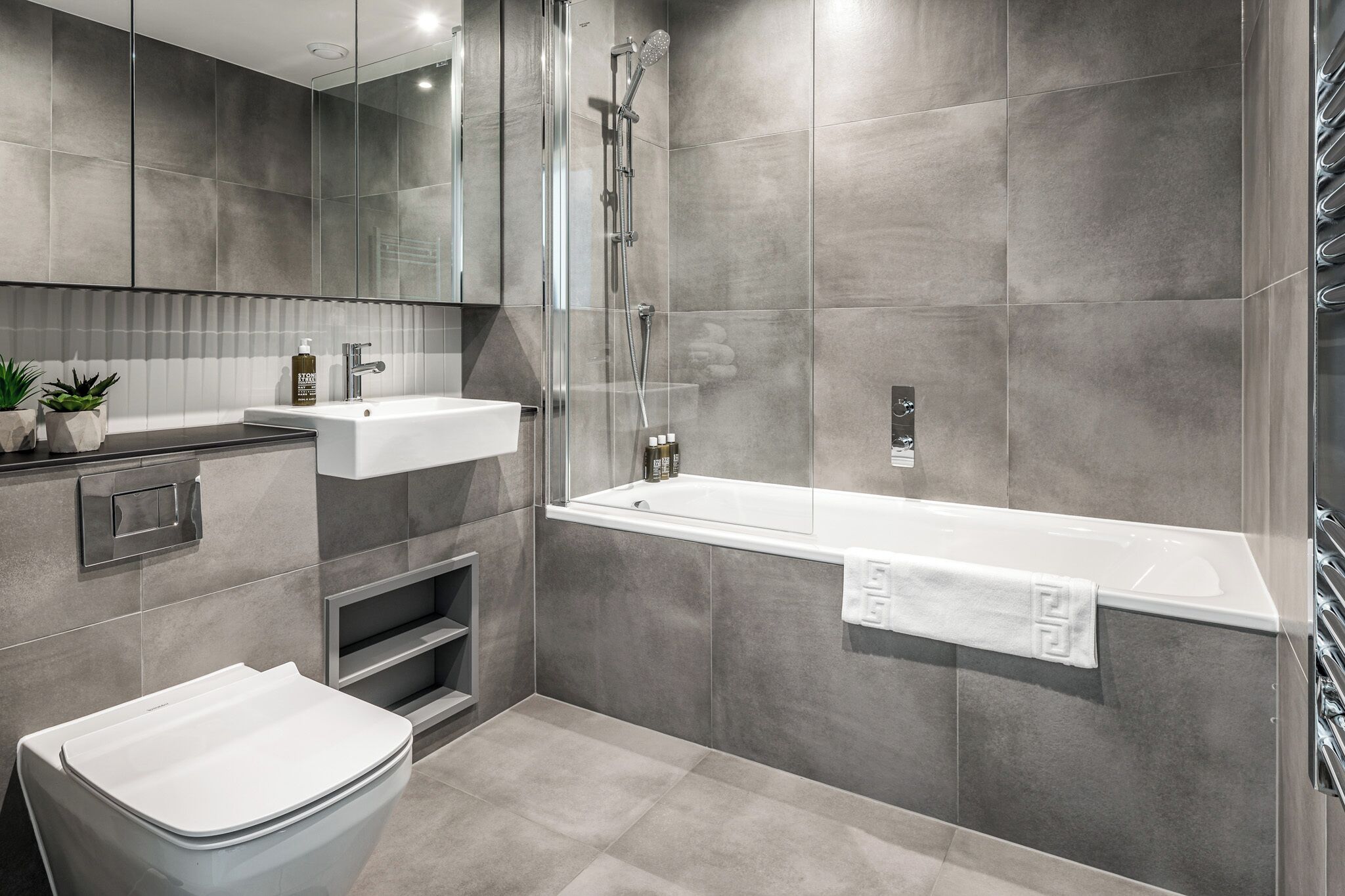 A modern bathroom with a glass-enclosed shower, a white bathtub, and a sink with a mirror above.
