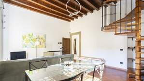 Un comedor con mesa de vidrio, sillas de mimbre, un sofá y una escalera con barandilla de madera.