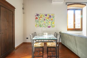 Un comedor con mesa de vidrio, sillas de mimbre y un cuadro floral colorido en la pared.