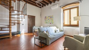 Una sala de estar con una escalera de madera, un sofá, una mesa de centro y una ventana con vistas.