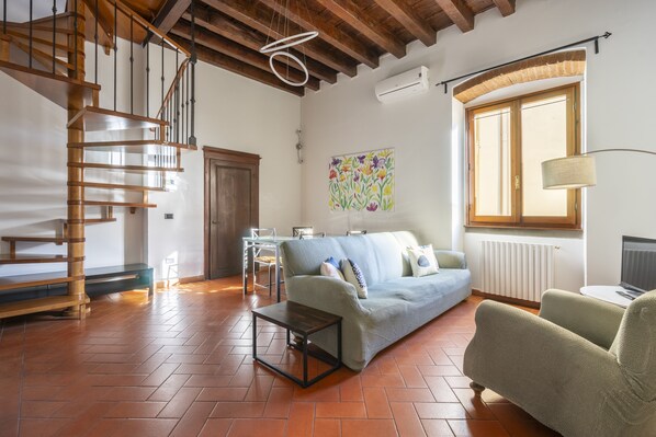 Una sala de estar con una escalera de madera, un sofá, una mesa de centro y una ventana con vistas.