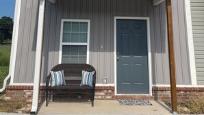 Une maison à deux étages, avec une façade grise, un porche à l’avant doté d’un banc et une porte bleue.