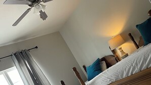 Une chambre à coucher avec un lit en bois, un ventilateur de plafond, une lampe de chevet et une fenêtre avec des rideaux.