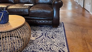 Un salon spacieux avec un canapé en cuir, une table basse ronde et un tapis à motifs.