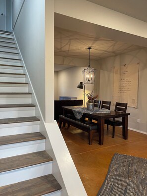A staircase leading to a dining area with a table set for four, a hanging light fixture, and a wall with a framed quote.
