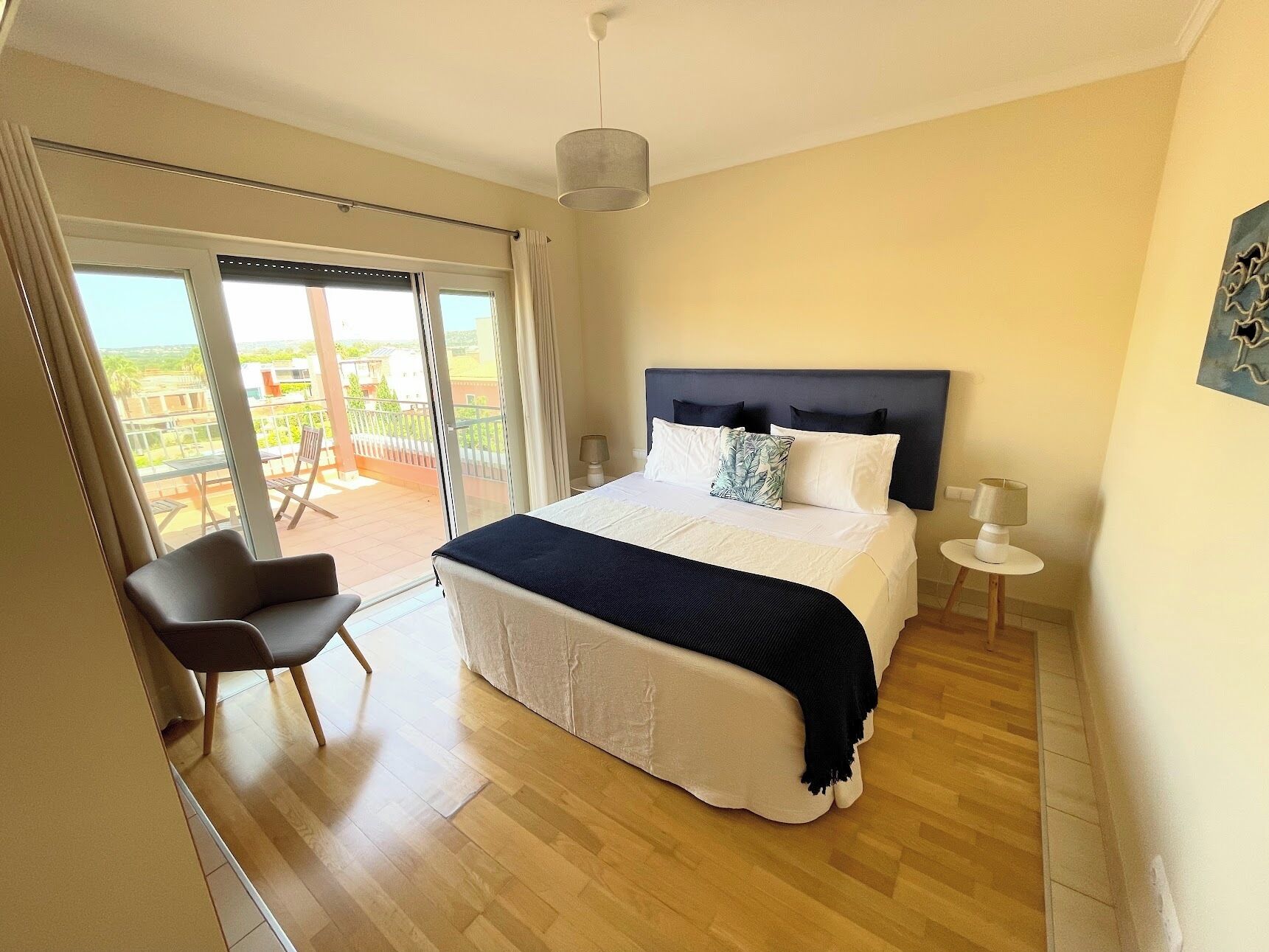 A bedroom with a large bed, a chair, a nightstand, and a view of the outdoors through a sliding door.