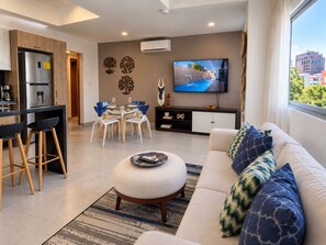 A modern living room with a sofa, ottoman, and a flat-screen TV mounted on the wall. - Unique location, workspace, great guest service (Santo Domingo)