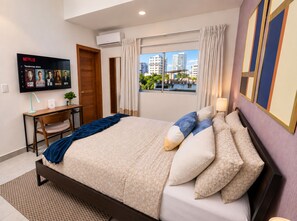 Une chambre d’hôtel équipée d’un lit, d’un bureau, d’un téléviseur diffusant du contenu Netflix et d’une fenêtre donnant sur la ville.