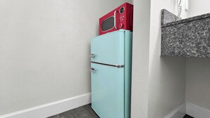 Un refrigerador pequeño azul claro con un microondas rojo encima, situado en una esquina de una habitación con paredes blancas y suelo de madera oscura.