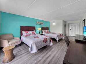 Habitació d'hotel amb dos llits, un sofà, una taula auxiliar petita i una televisió.