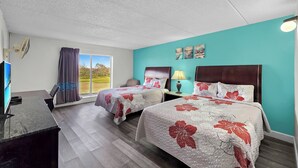 Habitación de hotel con dos camas, un escritorio, una silla, un televisor y un ventanal con cortinas.