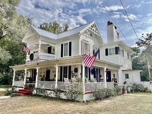 Une grande maison blanche avec un porche, de nombreuses cheminées et des drapeaux américains.