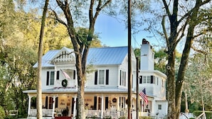 Une grande maison blanche de style colonial, dotée d’une véranda qui fait le tour de la maison, de plusieurs cheminées et de drapeaux américains.