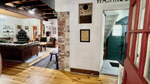 Une pièce chaleureuse avec un plancher en bois, un canapé en cuir marron, une petite table et un mur blanc sur lequel est affiché un panneau indiquant les « TOILETTES ».