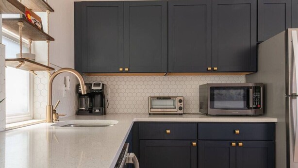 Une cuisine moderne avec des meubles de rangement de couleur sombre, un four à micro-ondes, un grille-pain et un lave-vaisselle.