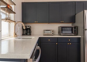 Una cocina moderna con armarios oscuros, microondas, tostadora y lavavajillas.
