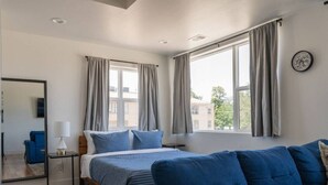 Une chambre à coucher avec un lit, un canapé bleu, un miroir et une fenêtre avec des rideaux.