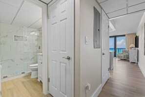Une chambre d’hôtel avec salle de bain, un balcon donnant sur la mer et un espace de vie comprenant un canapé et un téléviseur.