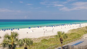 A beach with white sand, clear turquoise water, and a pier in the distance. - Hart of the Sea: 3rd floor, remodeled, beachfront, stylish, incredible amenities (Panama City Beach)