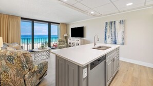 A modern living room with a kitchen island, a flat-screen TV, and a view of the beach. - Hart of the Sea: 3rd floor, remodeled, beachfront, stylish, incredible amenities (Panama City Beach)