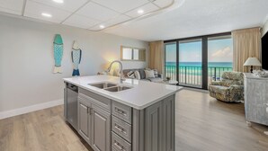 A modern kitchen with a central island, a dining area with a view of the ocean, and a balcony with a view of the beach. - Hart of the Sea: 3rd floor, remodeled, beachfront, stylish, incredible amenities (Panama City Beach)