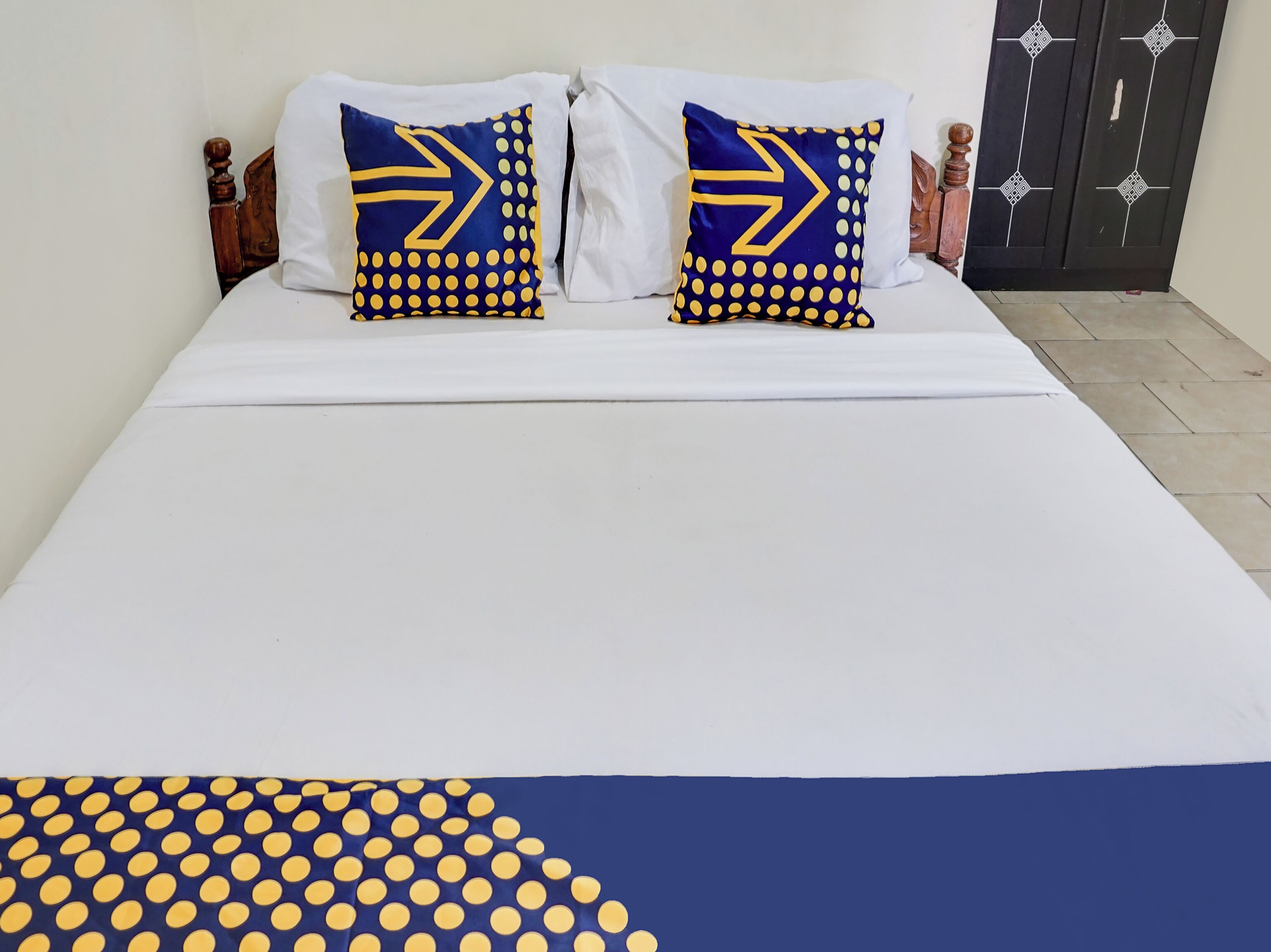 Ein Bett mit weißer Bettwäsche und zwei Kissen mit blauen und gelben Mustern.