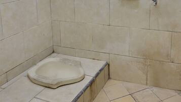 A small, tiled bathroom with a squat toilet and a soap dish on the wall.