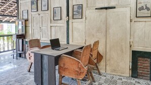Una habitació amb sòl de rajola, taula de fusta amb caires i un ordinador portàtil, i quadres a la paret.