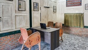 Habitació amb terra de rajola, escriptori amb un portàtil, dues cadires de fusta i una paret de maó.