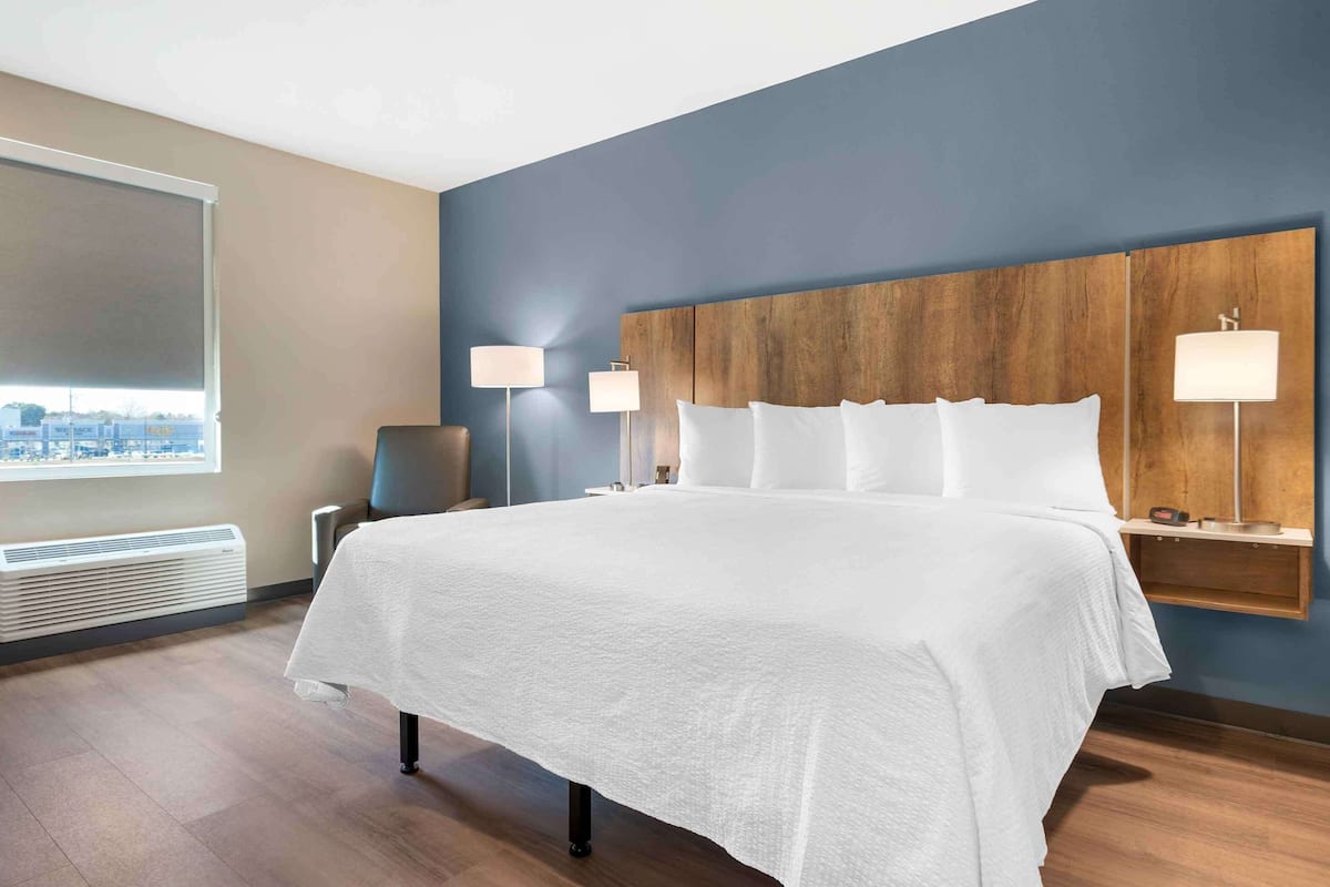 Una habitación de hotel con una cama grande, dos lámparas de noche, un cabecero de madera, un ventanal con vistas y un equipo de aire acondicionado integrado.