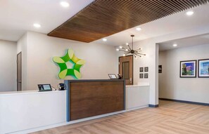Un espace d’accueil au design moderne, comprenant un comptoir d’accueil en bois, une œuvre d’art murale originale aux couleurs verte et jaune, et un luminaire contemporain.