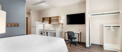 A hotel room with a bed, desk, chair, TV, wardrobe, and a small kitchenette.