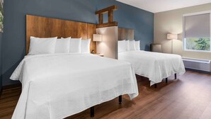 Habitación de hotel con dos camas, cabecero de madera, mesita de noche, lámpara y ventana con vistas.
