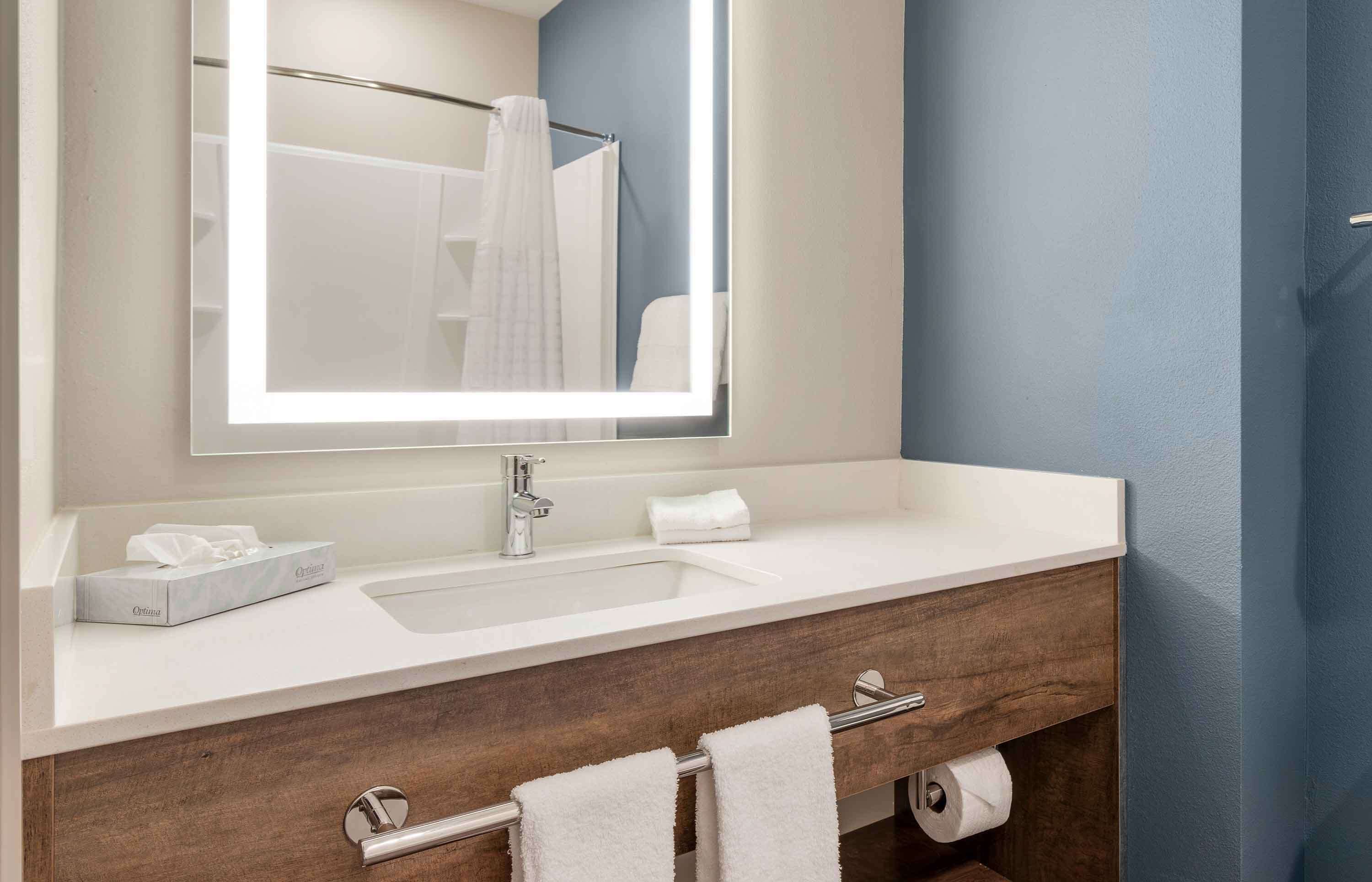 A bathroom with a white sink, a mirror, a towel rack, and a wooden vanity.