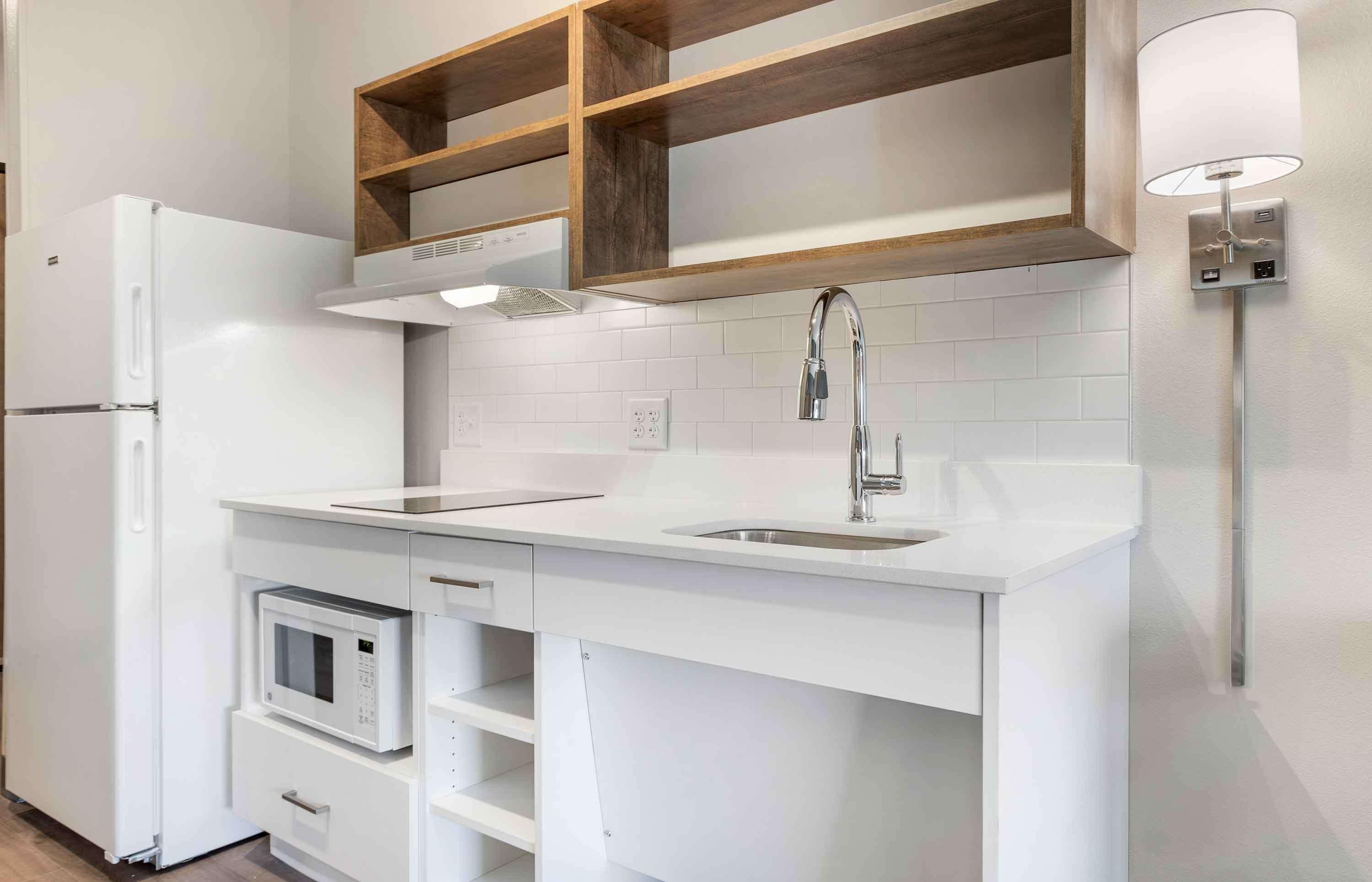 Een moderne keuken met witte kastjes, een ingebouwde magnetron, een roestvrijstalen spoelbak en een houten plank boven het aanrecht.