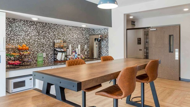 Una cocina moderna con una amplia mesa de madera y sillas de cuero marrón, un microondas y una cafetera.