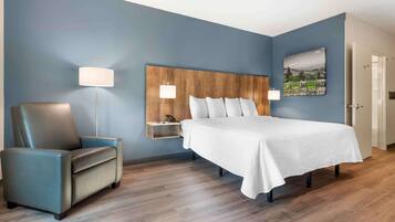 A hotel room with a bed, a chair, a nightstand, and a lamp.