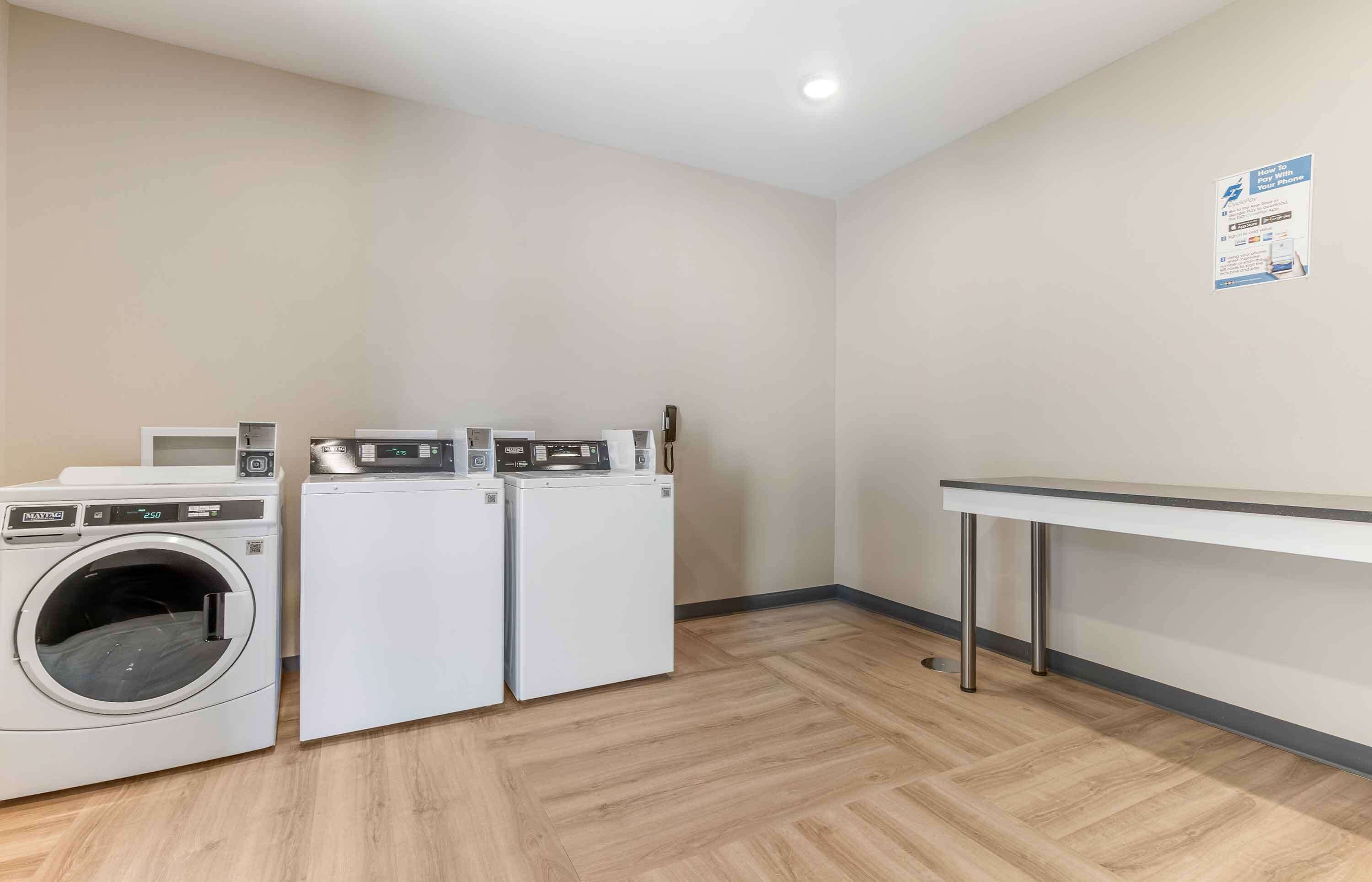 A laundry room with two washing machines and a drying machine, a table, and a wall-mounted sign.