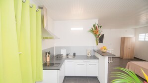 A compact kitchen with white cabinets, a sink, and a countertop. There is a small dining area with a table and chairs. - La Santa Clara - Studio climatisé (Saint-Pierre)