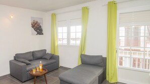 A modern living room with a grey sofa, a smaller grey couch, and a round wooden table with a bottle and glass. - La Santa Clara - Studio climatisé (Saint-Pierre)