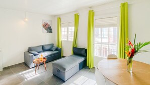 A modern living room with a grey sofa, a small round table, and bright green curtains. - La Santa Clara - Studio climatisé (Saint-Pierre)