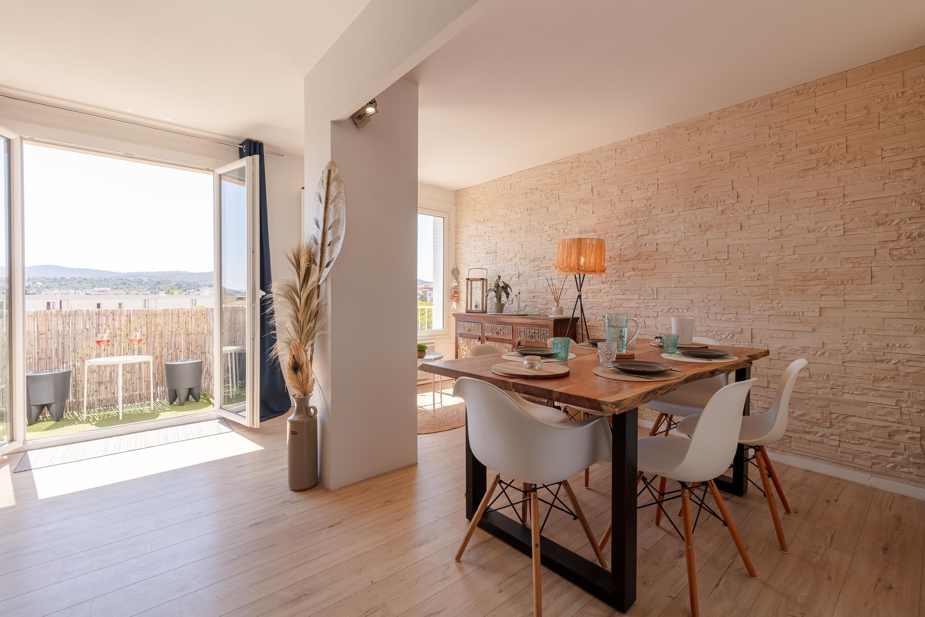 Un comedor con una mesa de madera, sillas blancas y una pared de ladrillo.
