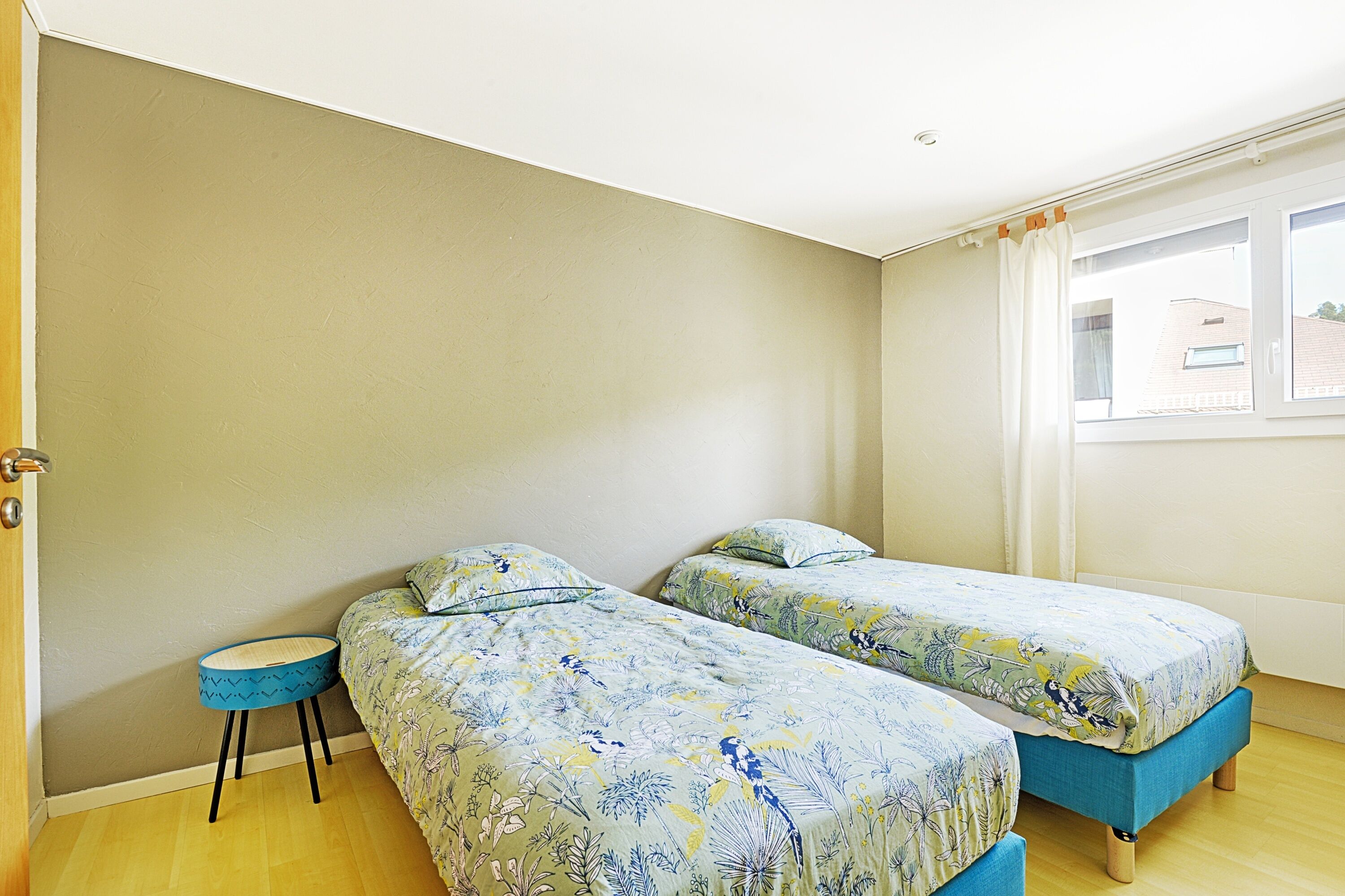 Un dormitorio con dos camas, una mesita redonda y una ventana con cortinas.
