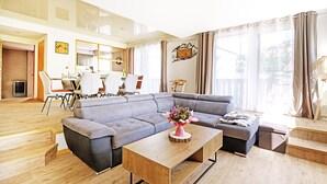 Una sala de estar moderna con un sofá seccional gris, una mesa de centro de madera con un florero y una zona de comedor al fondo.